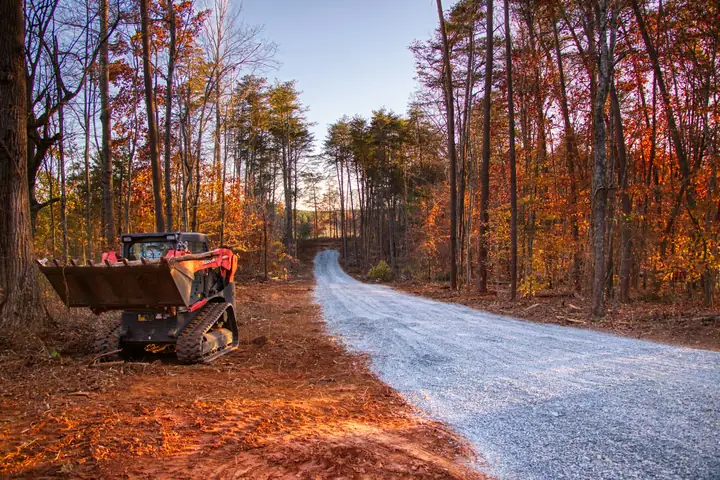 Track loader beside a new gravel road through autumn woods