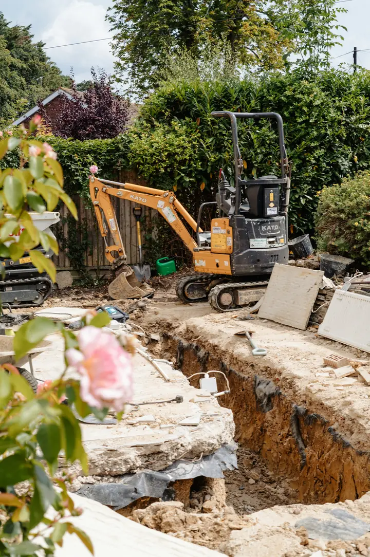 Mini excavator beside a freshly dug trench in a backyard