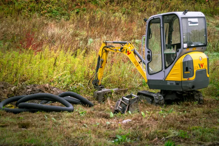 Compact excavator beside coiled drain pipe in a grassy field